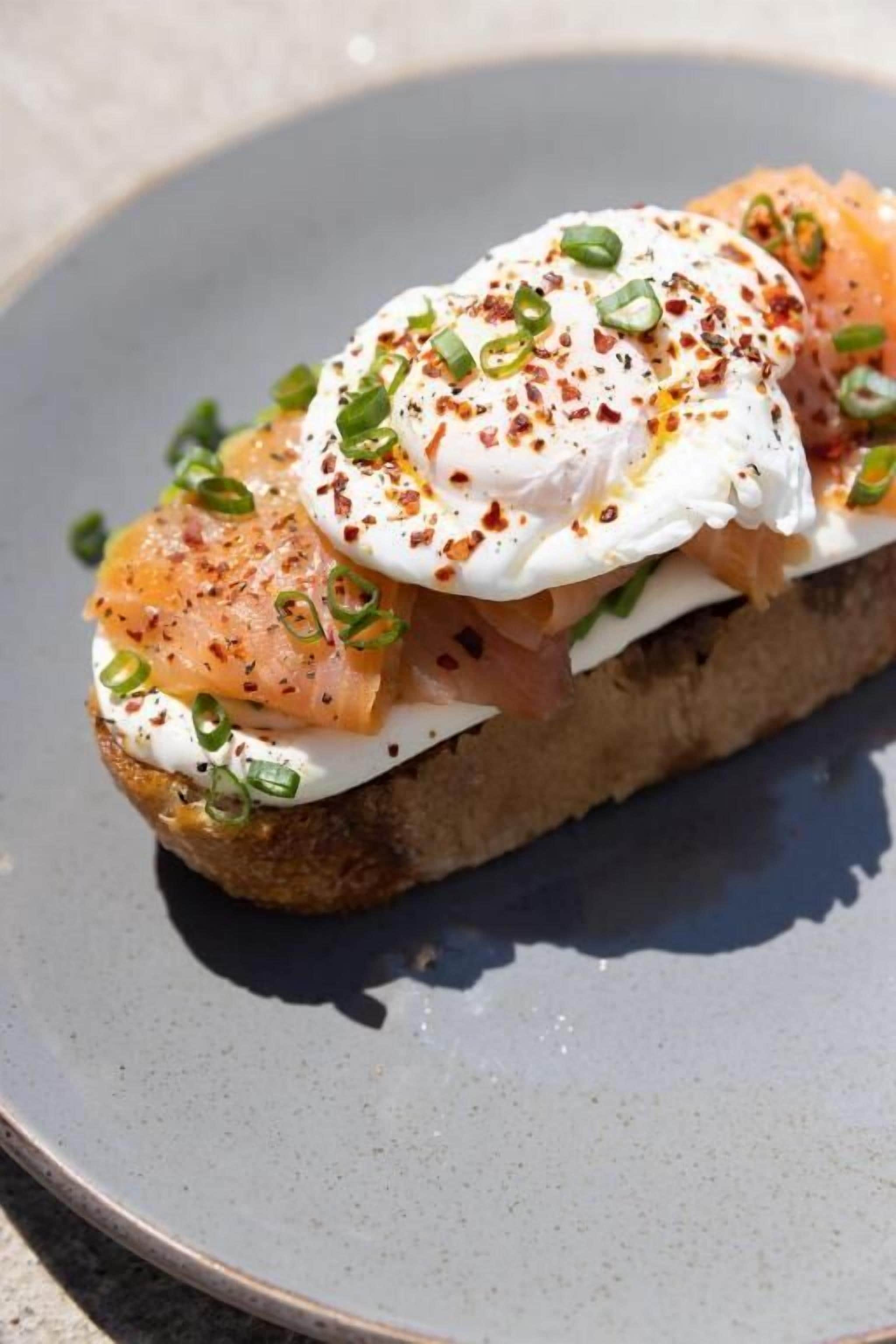 A sandwich with smoked salmon, a poached egg, and green onions on a slice of bread.