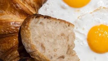 A croissant, two slices of bread, and two fried eggs on a wooden surface.