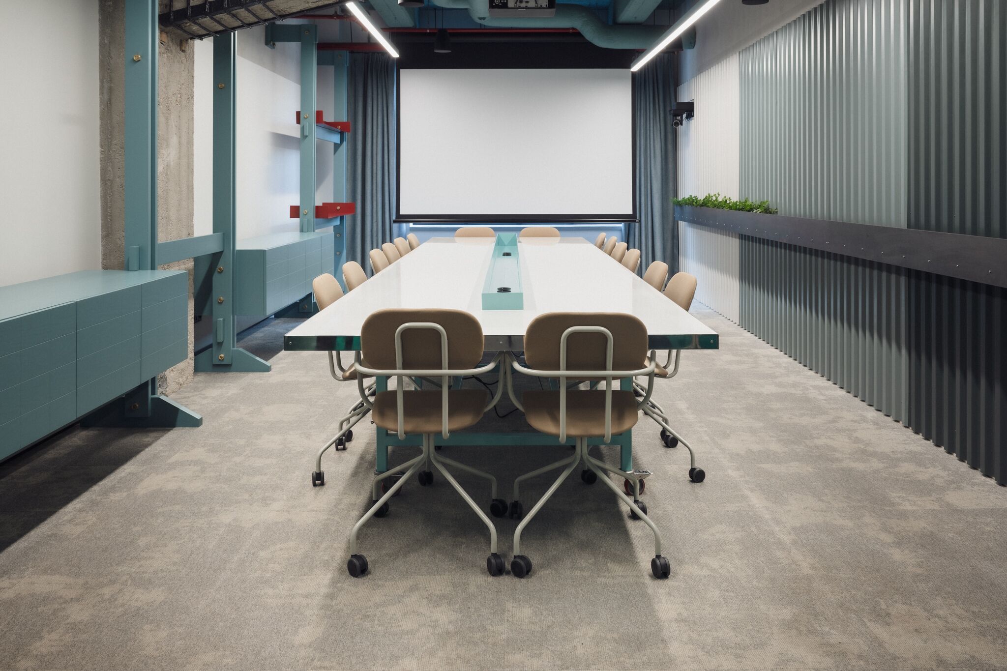 A conference room with a long table, chairs, and a projector screen.