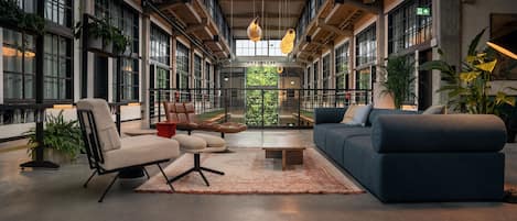 Un interior espacioso y moderno con techos altos, ventanas amplias y una variedad de zonas de estar con sofás y sillones.