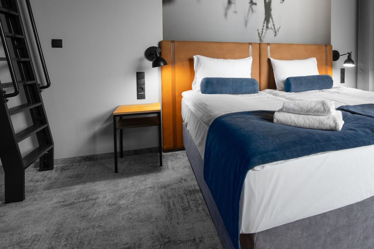 A hotel room with a bed, bedside table, lamp, and a view of the outside.