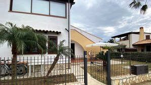 Una casa a due piani con un patio in pietra, un giardino recintato e una palma.