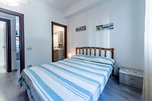 Quarto com cama, mesa de cabeceira, espelho e duas quadros na parede.