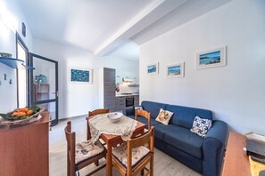 Uma sala de estar moderna com área de jantar, um sofá azul e uma cozinha ao fundo.