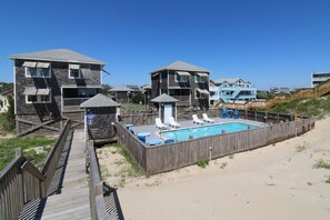 Une propriété située en bord de mer, dotée d’une terrasse en bois, d’une piscine et de plusieurs bâtiments.
