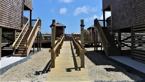 Una passerella in legno che conduce a case sulla spiaggia con balconi e ringhiere.