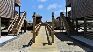 A wooden boardwalk leading to beach houses with balconies and stairs. - Whalebone Oceanside 3 Bedroom Cottage A (Nags Head)
