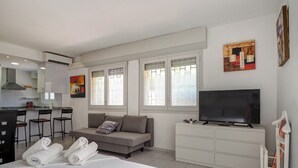 Une chambre d’hôtel équipée d’un lit, d’un canapé, d’une télévision, d’un petit coin cuisine et d’une fenêtre avec des stores.