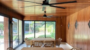 Un espace de repas moderne avec un plafond en bois, un ventilateur de plafond et de grandes fenêtres offrant une vue sur l’extérieur.