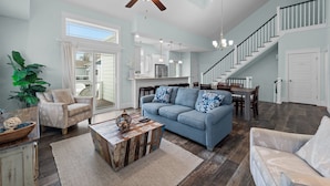 A spacious living room with a blue sofa, a wooden coffee table, and a ceiling fan. - Home on the Banks at Beacon Villas 4 Bedroom Townhouse (Corolla)