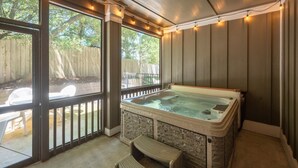 Un bain à remous avec un revêtement extérieur en pierre, une terrasse en bois et une vue sur une clôture en bois et des arbres.
