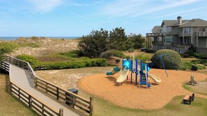 Un terrain de jeux avec des toboggans et une terrasse en bois donnant sur une plage.