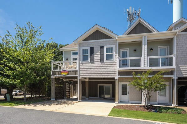 A two-story building with a balcony, a garage, and a small tree in the front yard.