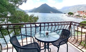 Un balcon avec une table et des chaises donnant sur un lac, avec une montagne en arrière-plan.