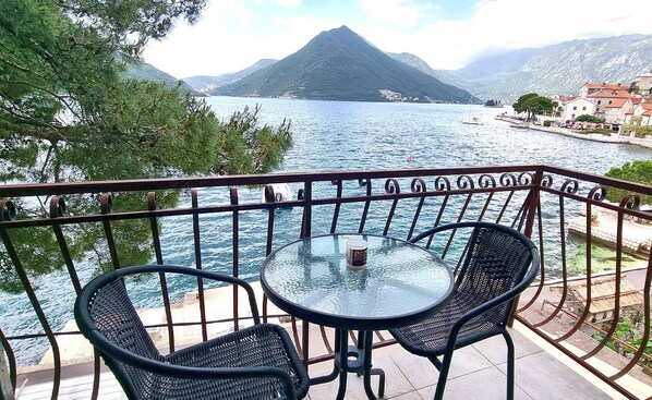 A balcony with a table and chairs overlooking a lake with a mountain in the background.