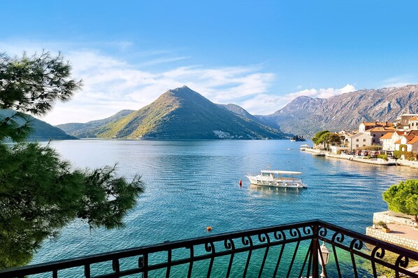Une ville côtière avec une montagne en arrière-plan, un bateau nommé « LUNA » sur l’eau et une balustrade de balcon.