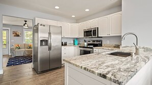 A modern kitchen with white cabinets, stainless steel appliances, and a granite countertop. - Amina's Cottage 3 BR in KDH + Pets Stay Free (Kill Devil Hills)