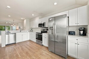 A modern kitchen with white cabinetry, stainless steel appliances, and a wooden floor.