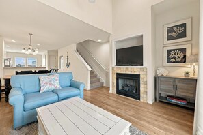 A living room with a blue sofa, a white coffee table, a fireplace, and a TV mounted above it.