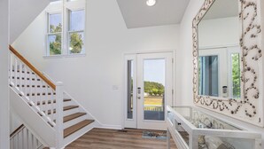 Ein Flur mit einer Holztreppe, einer Glastür zum Außenbereich und einem Spiegel mit Muschelbild.