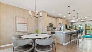 A modern kitchen with a central island, grey upholstered chairs, and pendant lighting. - Sea Therapy at Cambridge Cove (Kill Devil Hills)