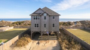 Une maison à deux étages avec vue sur la plage, une véranda et une allée menant à la maison recouverte de sable.