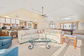 A spacious living area with a high ceiling, a ceiling fan, a pool table, a sofa, and a glass coffee table. - Hidden Gem 4 Bedroom Home in Hatteras (Hatteras)