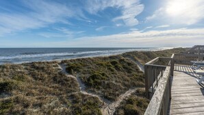 Une promenade en bois menant à une plage bordée de dunes et offrant une vue sur l’océan.