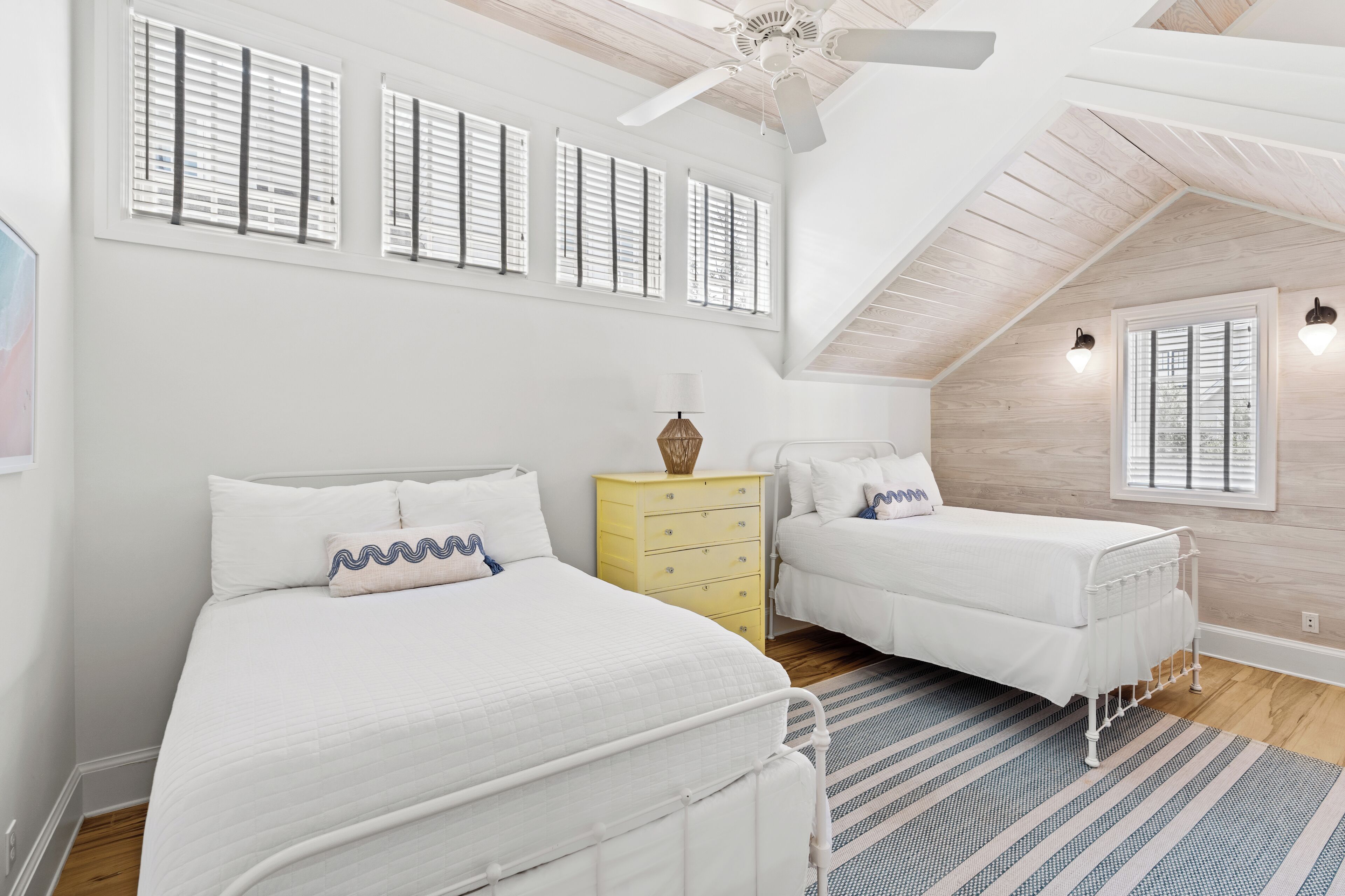 A bedroom with two beds, a ceiling fan, and a window with shutters.
