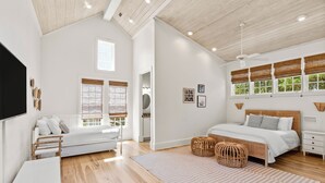 A spacious bedroom with a large bed, a sitting area with a sofa and a table, and a view of greenery through the windows. - Family Home | Beach Access | Private Guest House (Inlet Beach)