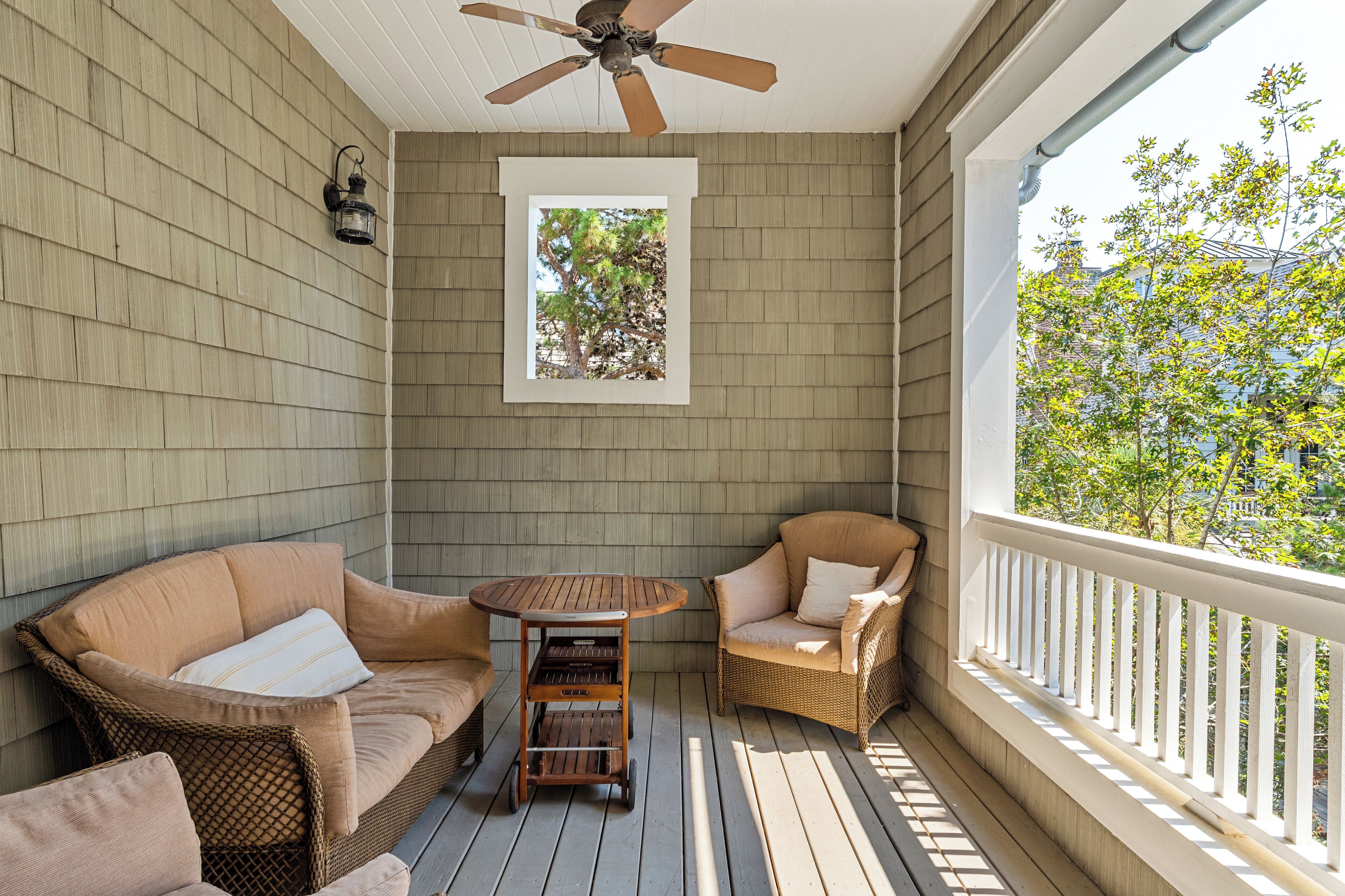 Eine überdachte Veranda mit Korbmöbeln, einem Deckenventilator und Blick auf Bäume.