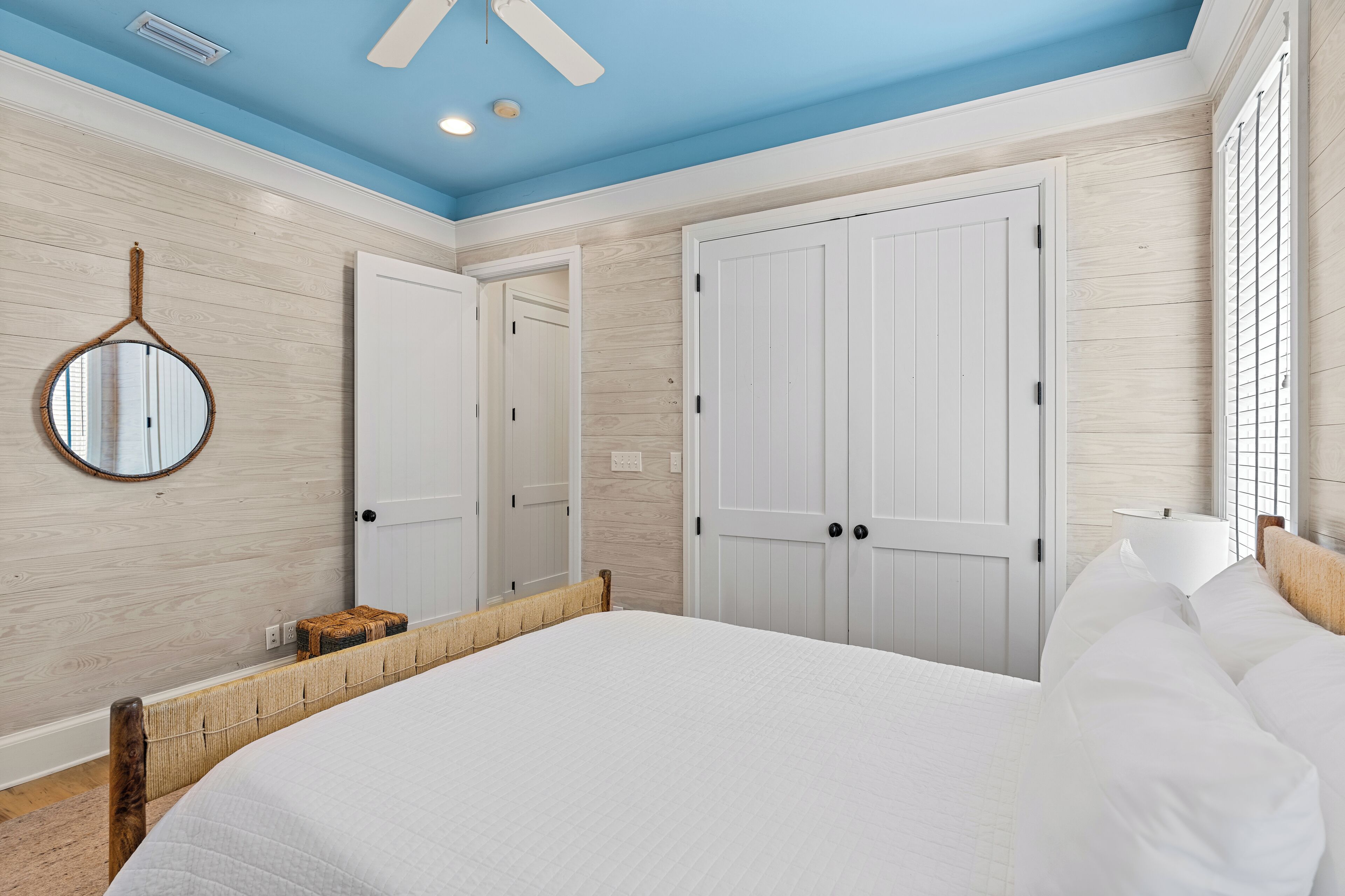 A bedroom with a large bed, wooden headboard, a round mirror, and white wardrobes.