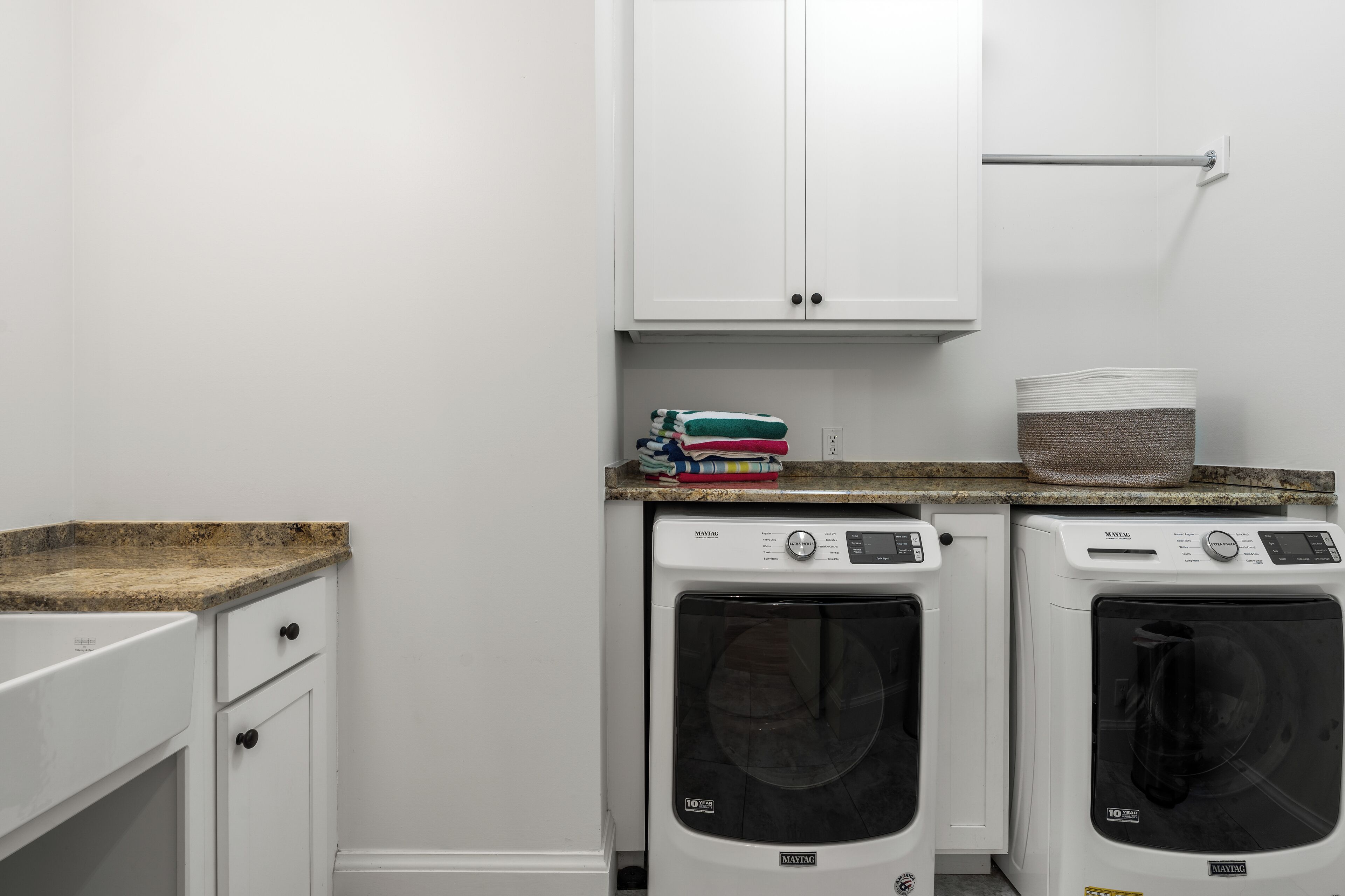 A laundry area with two Maytag washing machines, a countertop, a cabinet, and a towel rack.