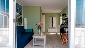 A compact living space with a blue sofa, a small white coffee table, and a kitchen area with a dining table and chairs. - Beachlodge by the Sea | Honeymoon suite on the beach (Wijk aan Zee)