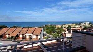 Vista costera desde un balcón con edificios de tejados de terracota, cielo despejado y el mar al fondo.