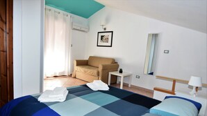 Habitación de hotel con cama, sofá, una mesita, un espejo y ventana con cortinas.