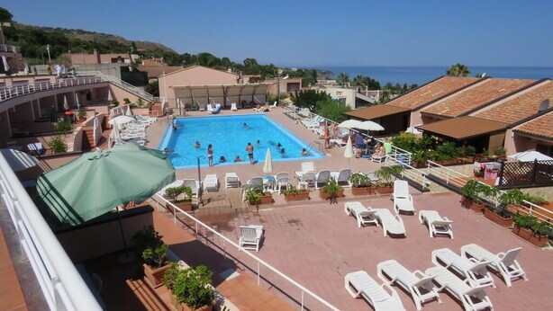 Un área de piscina en la azotea con sillones de descanso, una piscina y vistas al mar.