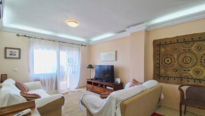 Ein Wohnzimmer mit zwei Sofas, einem Fernseher, einem Teppich und einem Wandbehang mit Muster.