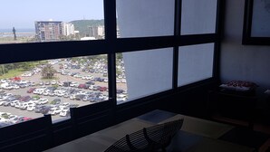 A room with a large window overlooking a parking lot and buildings. There is a bench with a cushion and a small table with a pillow. - Stunning 3-bed Apartment in Durban (Durban)