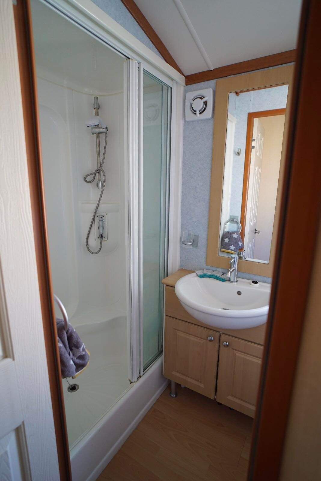 Een badkamer met een douche met glazen wand, een wastafel met spiegel en houten kastjes.