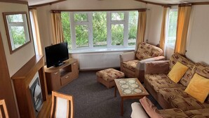 A cozy living room with a TV, sofa, and a window with curtains. - Cozy 2 Bedroom Coastal Chalet in Hunstanton (King's Lynn)