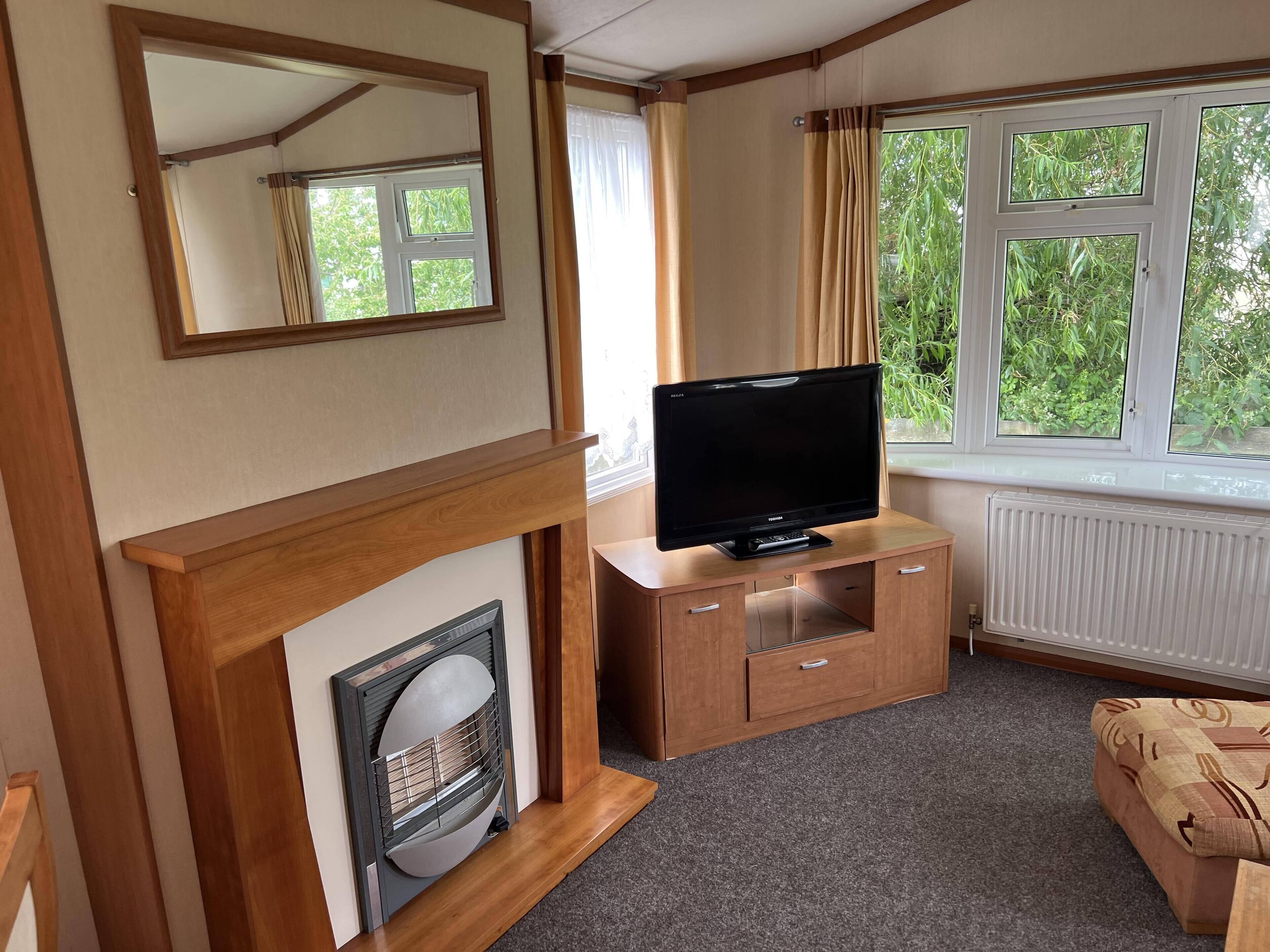 A cozy room with a fireplace, a television on a wooden cabinet, and a window with a view of greenery.