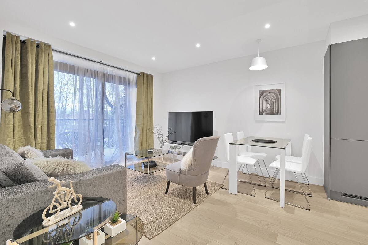 A modern living room with a sofa, a glass coffee table, a TV, and a dining area with white chairs.