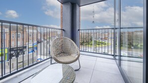 A balcony with a wicker chair and a glass table, offering a view of the street and buildings below. - Belmore 1 & 2 Bedroom Luxury Apartment (Stanmore)