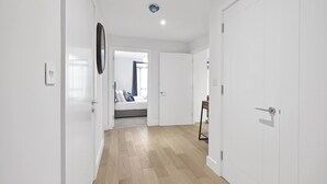 A hallway with white walls, wooden flooring, and a bed in the background. - Belmore 1 & 2 Bedroom Luxury Apartment (Stanmore)