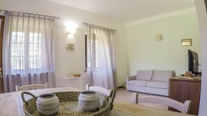 A living room with a dining table, two woven baskets, a sofa, and a television on a wooden stand. - SERENELLA, on the ground floor, overlooking the park, for 2/4 pers. (Camaiore)