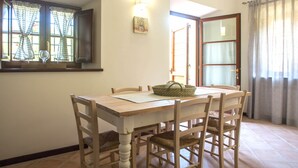 A dining area with a wooden table and chairs, a basket on the table, and a window with curtains. - SERENELLA, on the ground floor, overlooking the park, for 2/4 pers. (Camaiore)