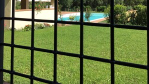 A view through a window with a grid pattern, featuring a swimming pool, green lawn, and a building with a tiled roof. - SERENELLA, on the ground floor, overlooking the park, for 2/4 pers. (Camaiore)