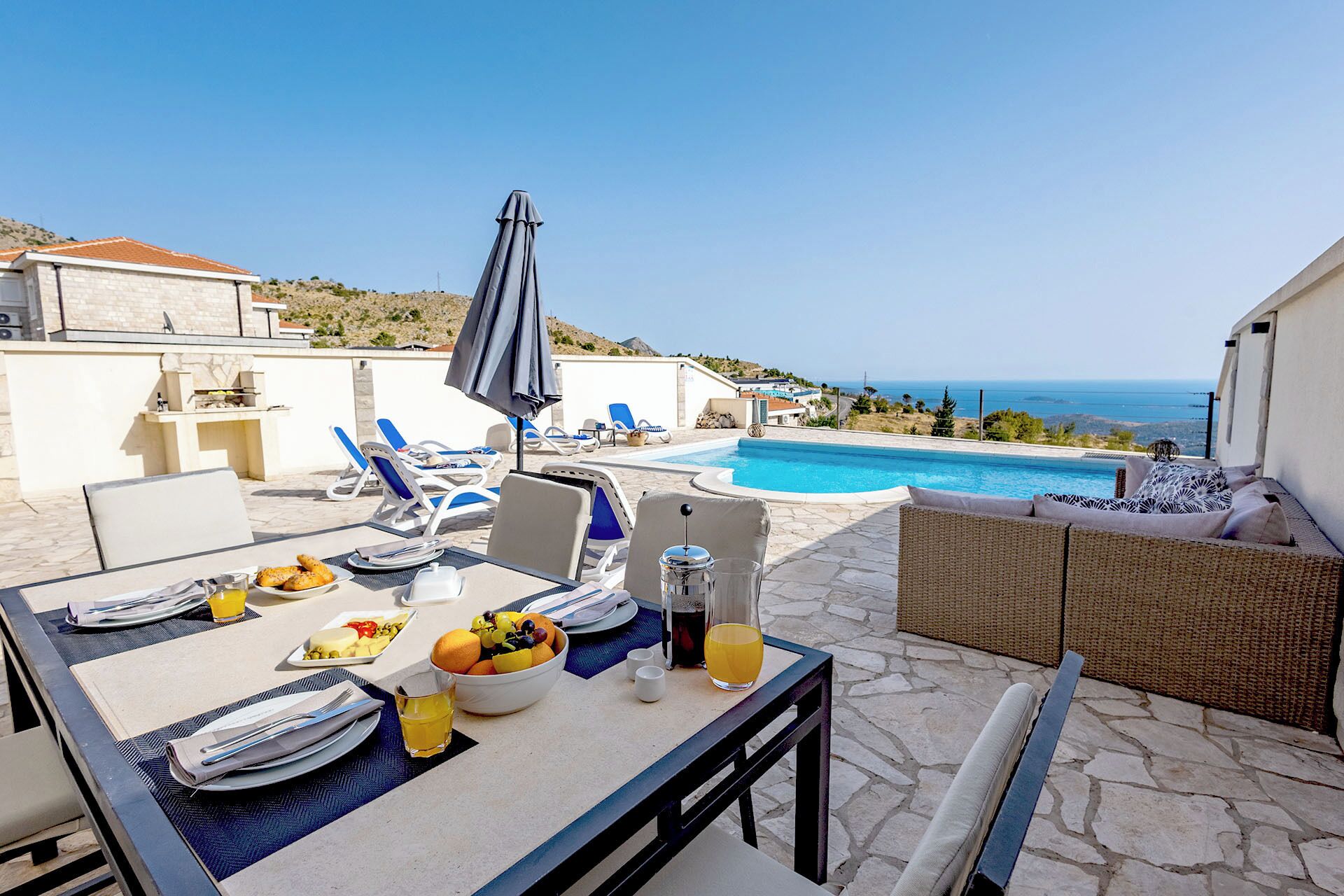 A patio with a dining table set for breakfast, a pool, and lounge chairs.