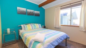 Een slaapkamer met een bed, een nachtkastje, een raam met gordijnen en een muur met drie berglandschappen.